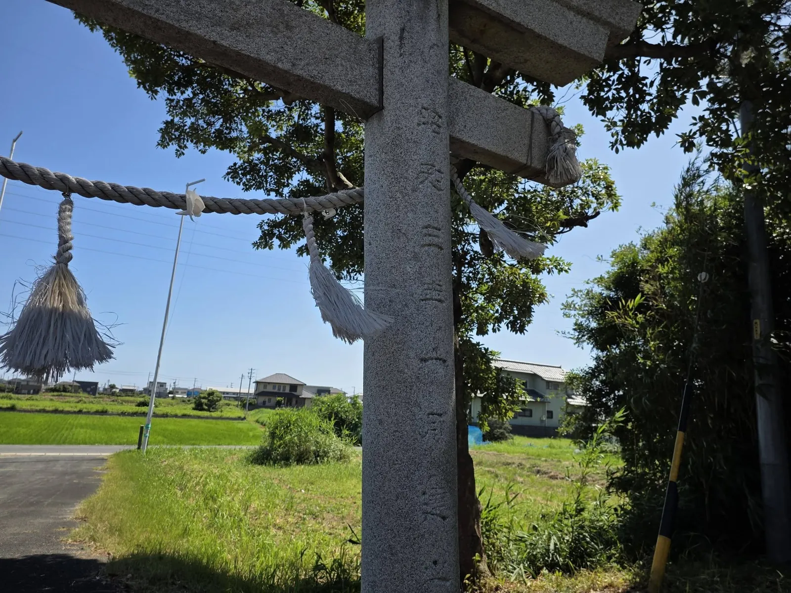 注連縄を掛けた石造鳥居と境内周辺の田園。