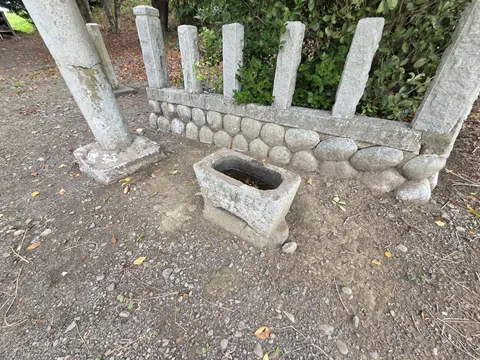 鳥居脇の石造手水鉢。背後の斜面には玉垣の石柱が並ぶ。