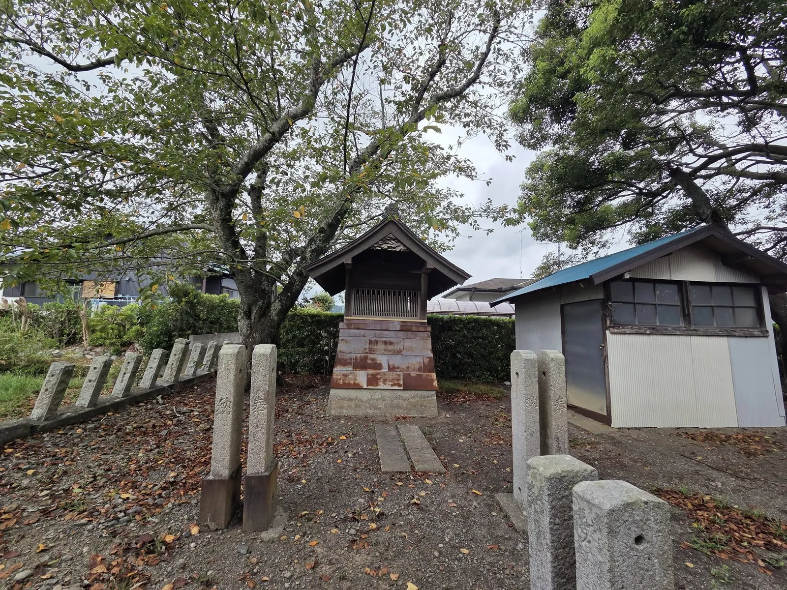 境内西側の小建物と玉垣。樹木に囲まれた境内の様子を示す。