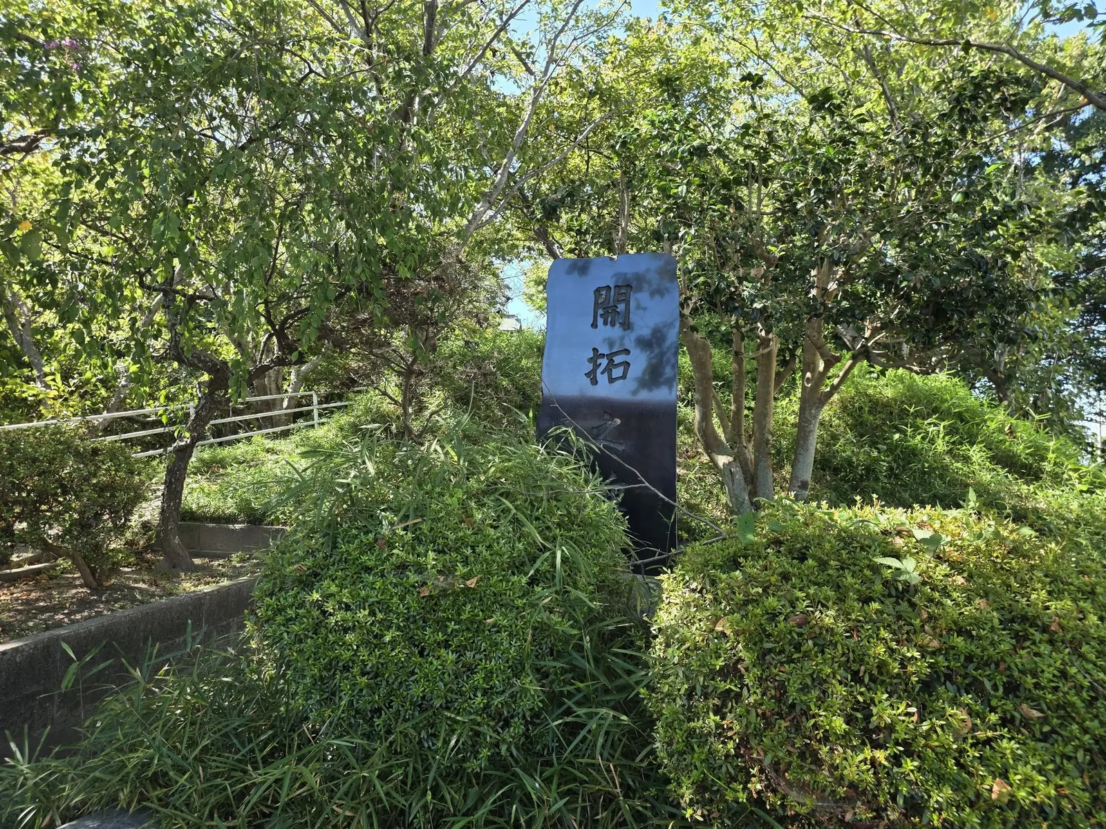 境内の植栽の中に立つ「開拓」の碑。