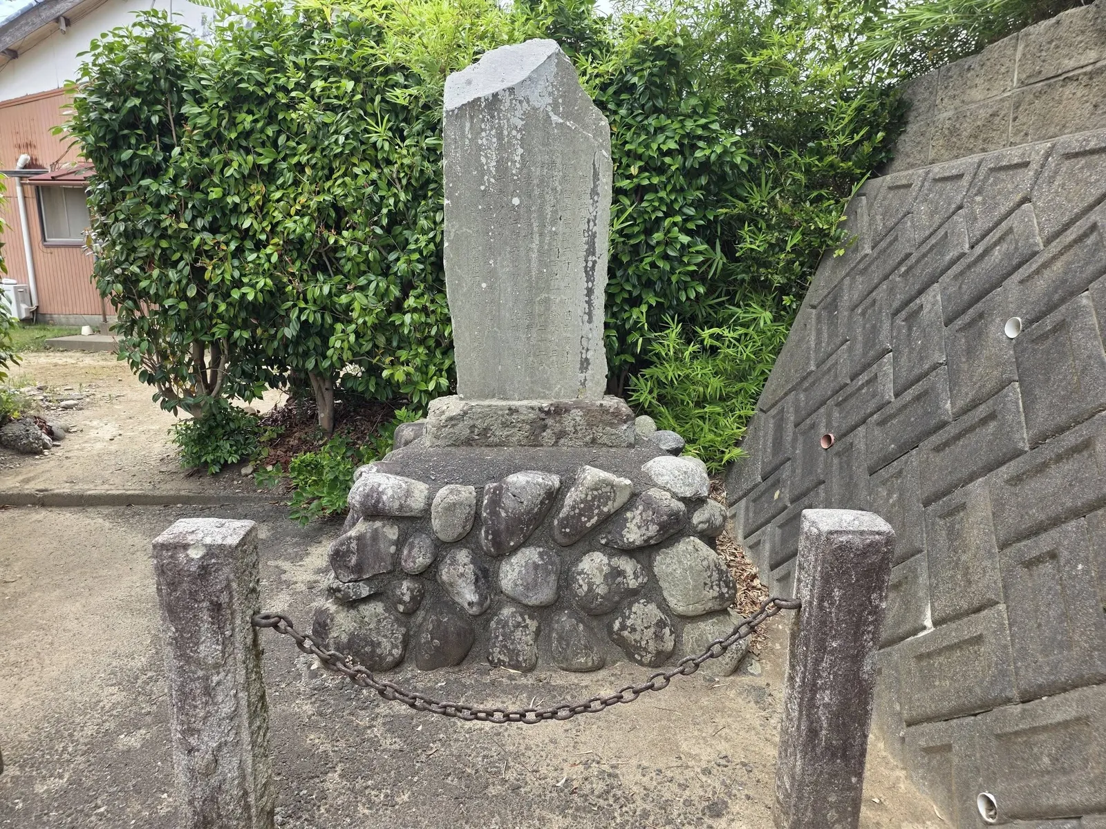 境内入口脇の石碑。玉石積みの基壇に立つ。