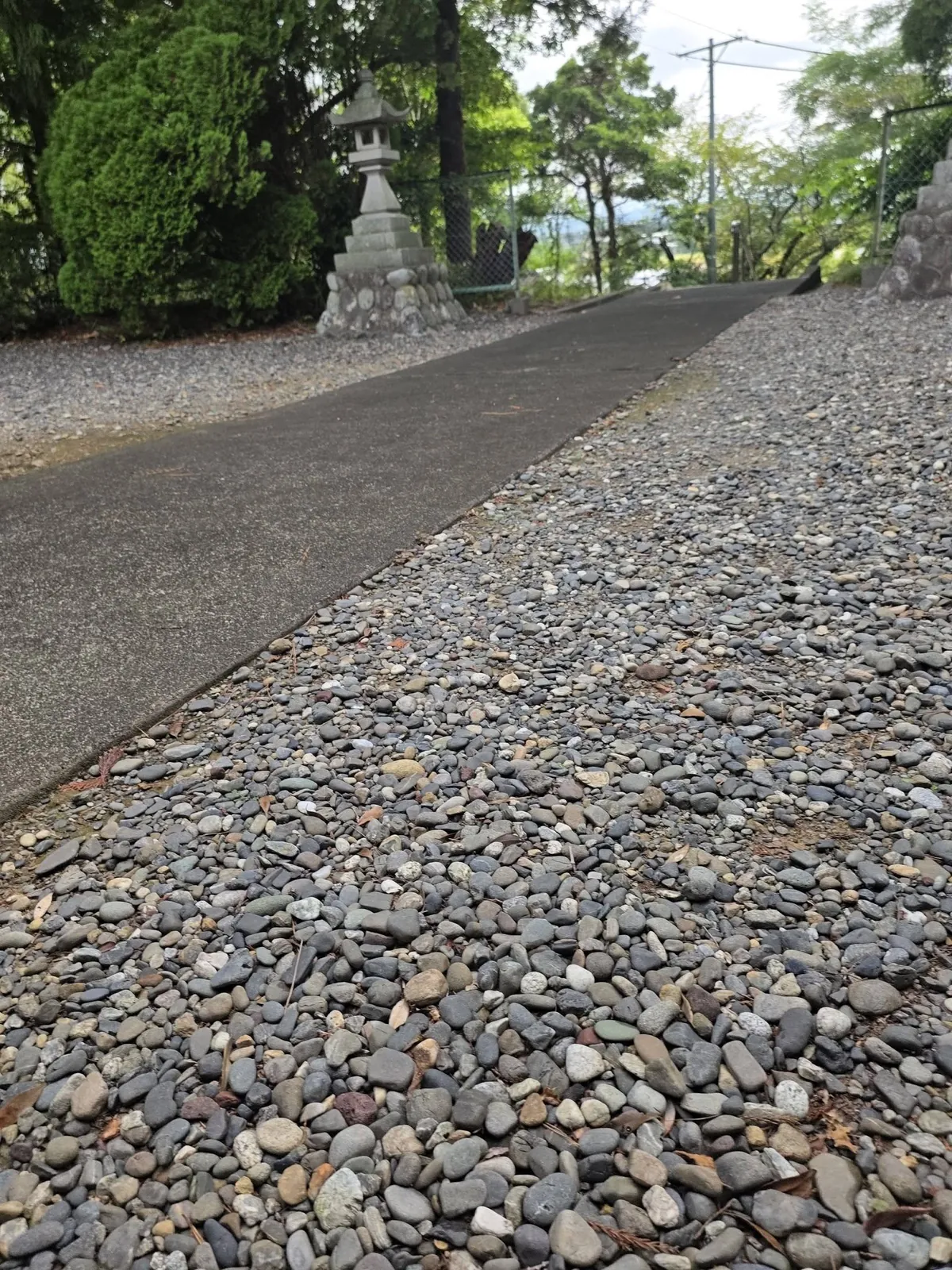 社殿前の砂利敷きから参道方向を見る。舗装された参道へ続く。