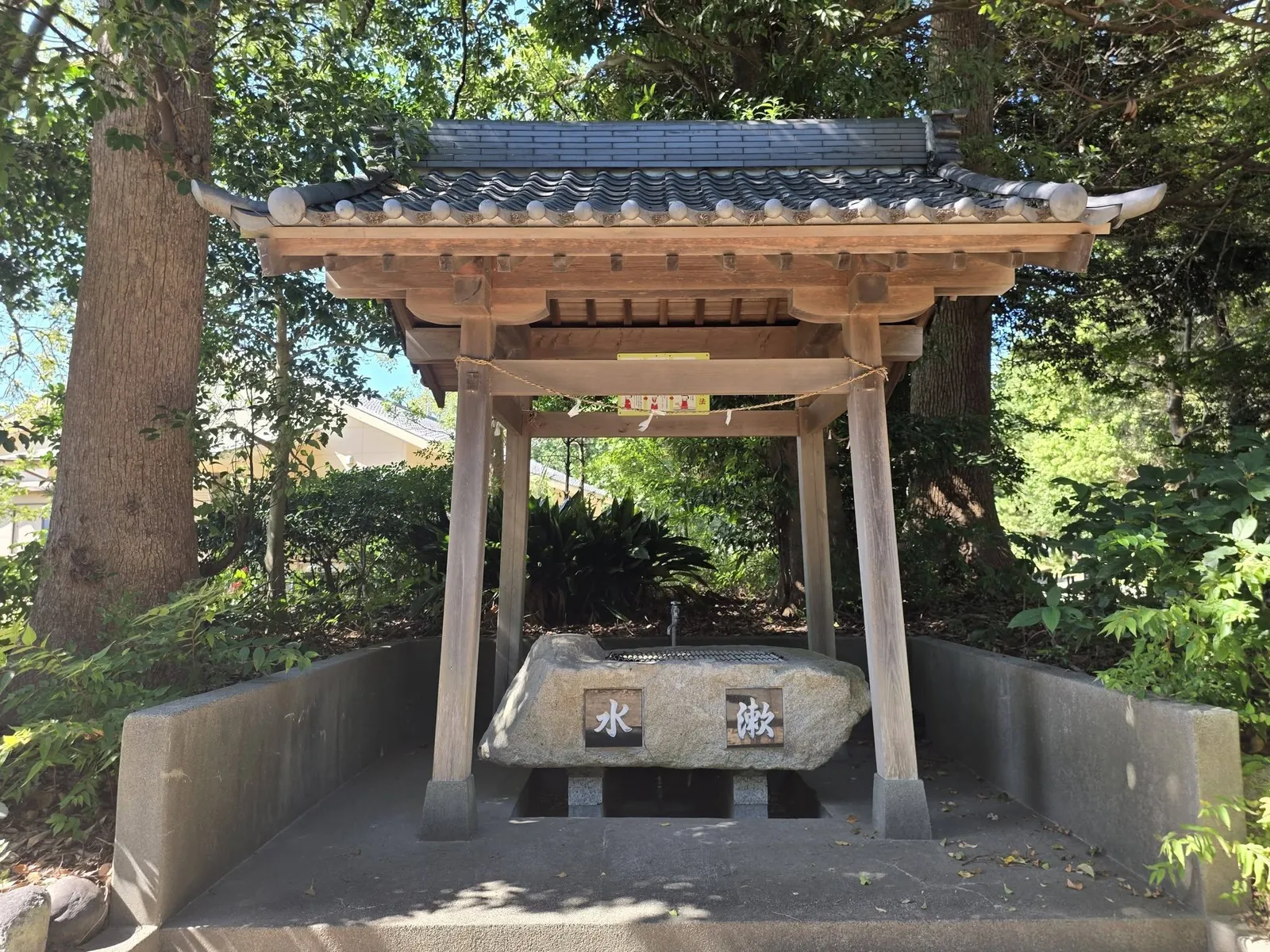 社叢の木々を背に建つ手水舎と手水鉢。