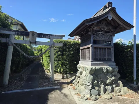 石造鳥居と参道入口。右手に木造の建物が立つ。