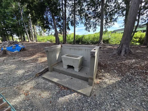 コンクリート造の覆屋の中にある石造の手水鉢。奥に玉石が積まれている。