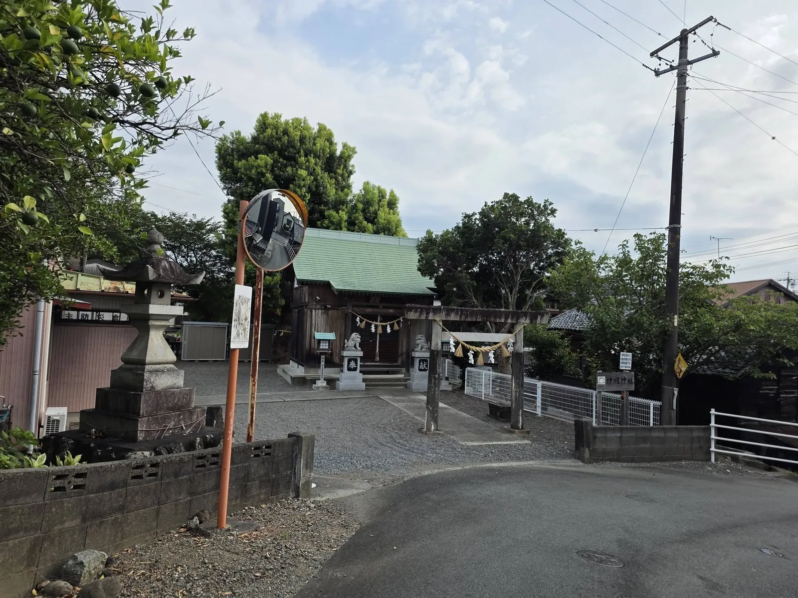前面道路から見た神明神社の境内。社叢の前に鳥居と社殿が見える。