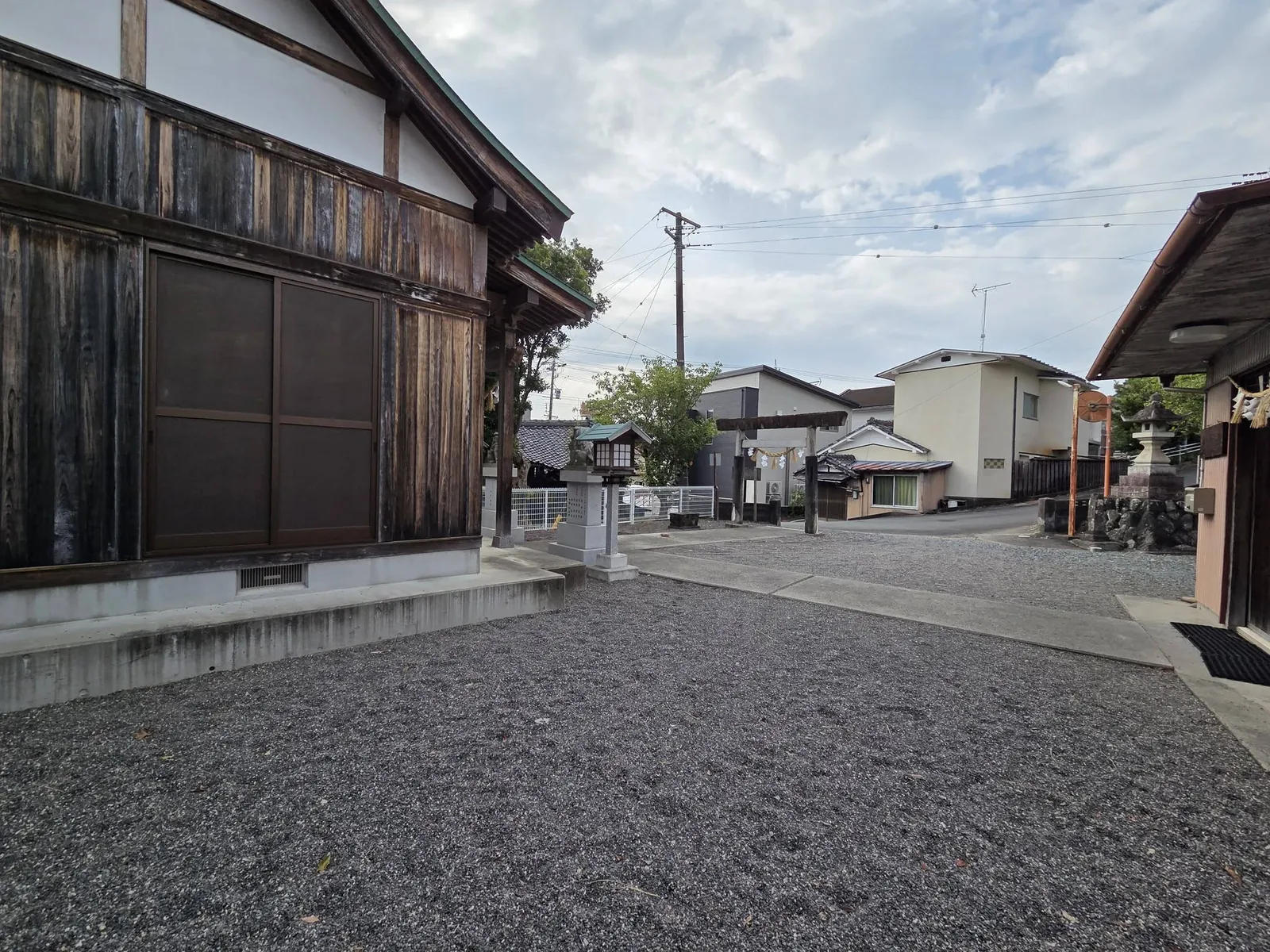 社殿を側面から見る。境内は砂利敷きで、前面道路に接する。