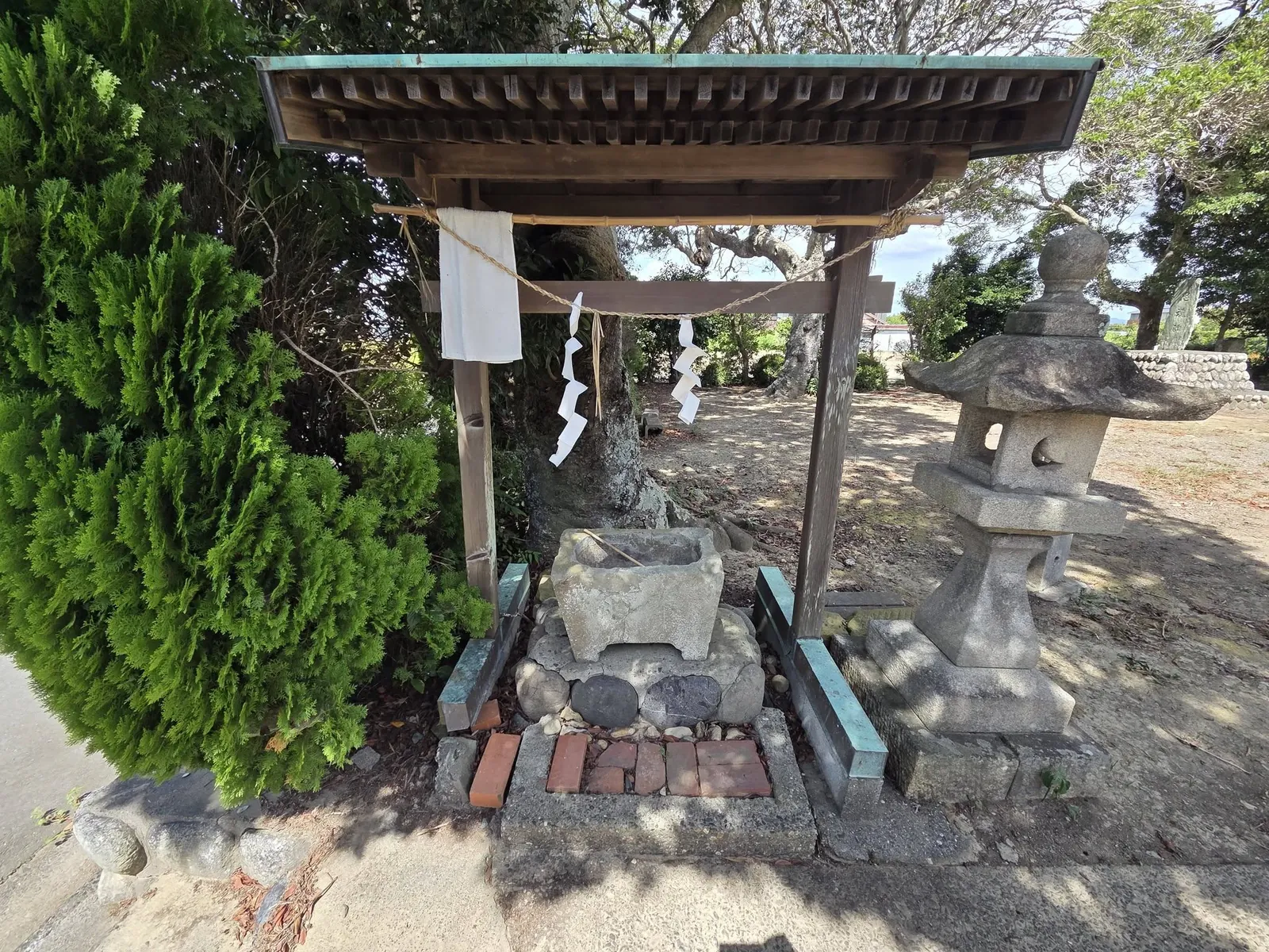 参道脇の手水舎。石造りの水盤に柄杓が渡され、右奥に石灯籠が立つ。