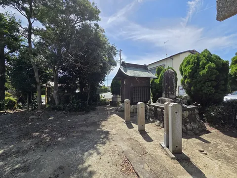 境内の一角にある小祠と石碑。奥に鳥居、右手に民家や道路が見える。