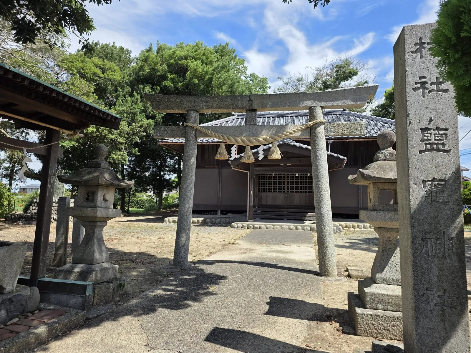 社号標「村社鹽竈神社」と石造鳥居、両脇の石灯籠。奥に社殿が見える。