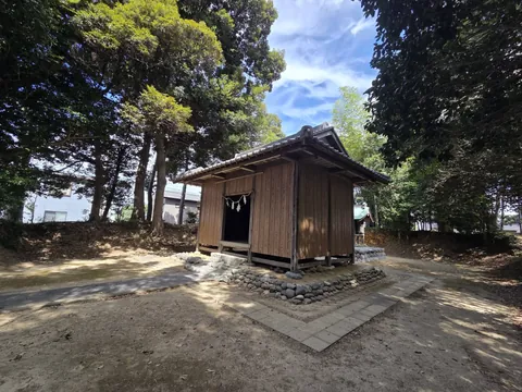 社殿を側面から見る。石積みの基壇に建ち、左奥に民家の屋根が望める。