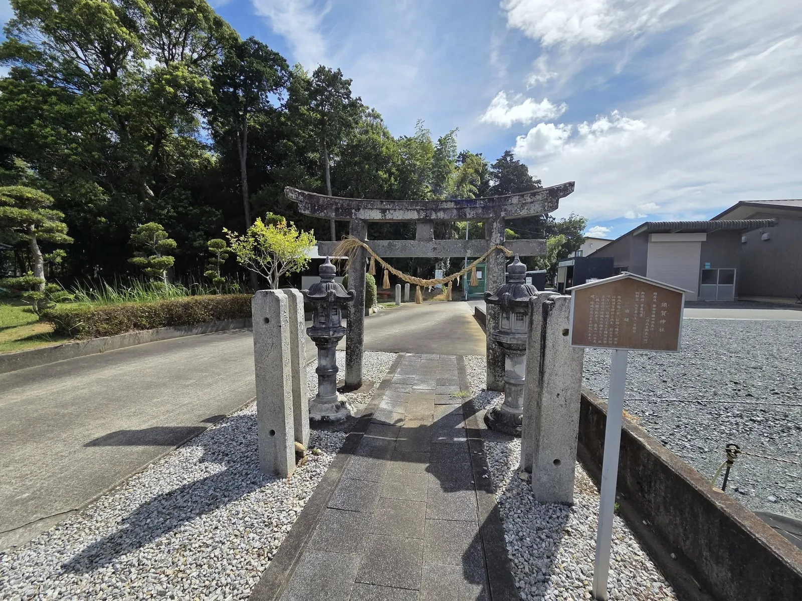 参道入口の石造鳥居。手前に灯籠と由緒板、奥に社叢が広がる。