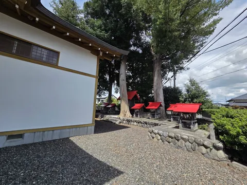 社殿の白壁と社叢の大杉の間から見た境内社の並び。奥に住宅街が広がる。