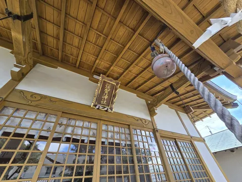 拝殿軒下に掲げられた「須賀神社」の扁額。銅製の鰐口と太い注連縄が下がる。