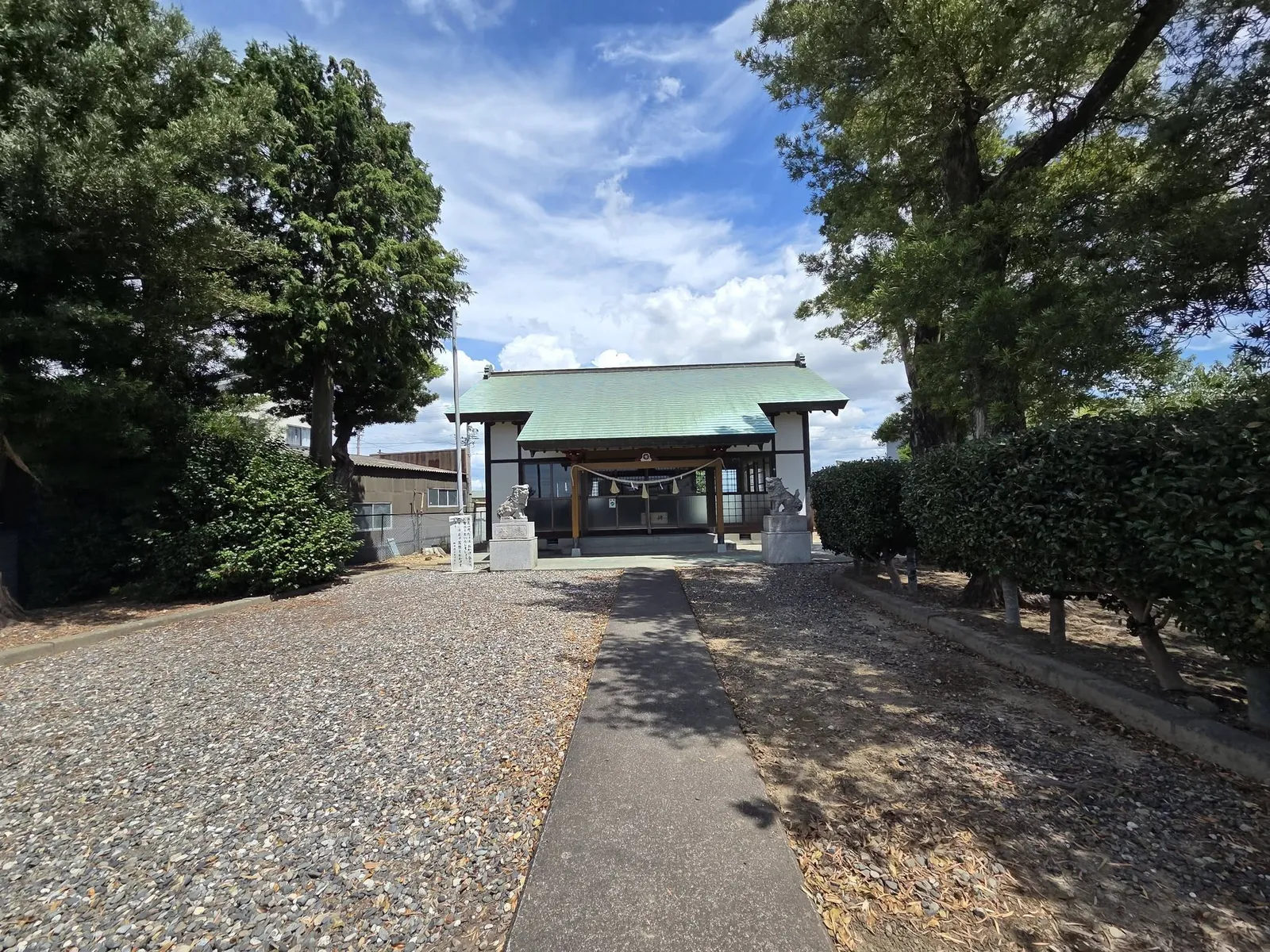 道路側から見た境内全景。社叢の中に社殿と一対の狛犬が見える。