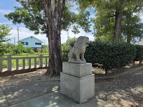 境内に立つ狛犬。台座の奥に民家が見える。