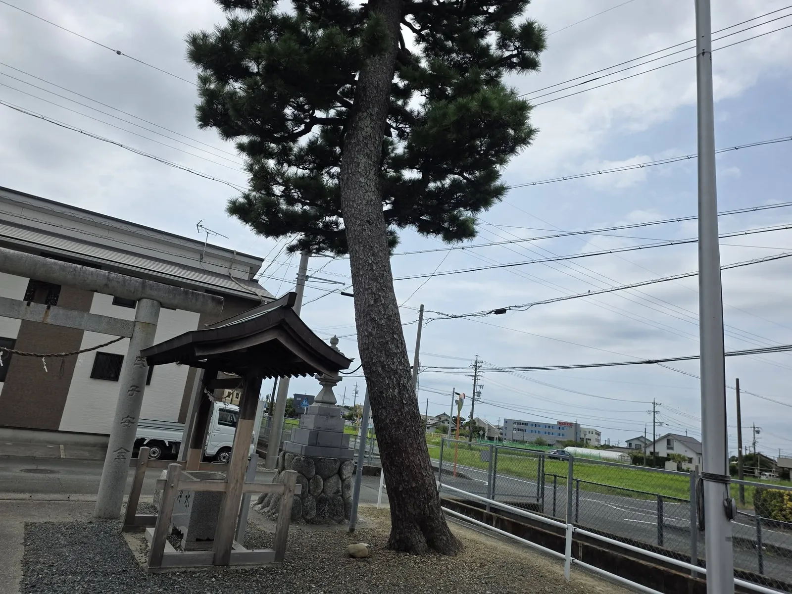 境内の手水舎と大木。社地は道路と水路に接する。