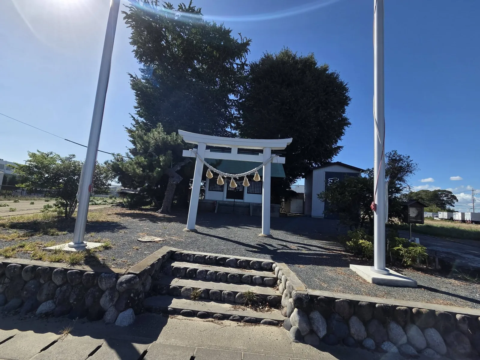 白い鳥居と幟竿の間から社殿を望む。