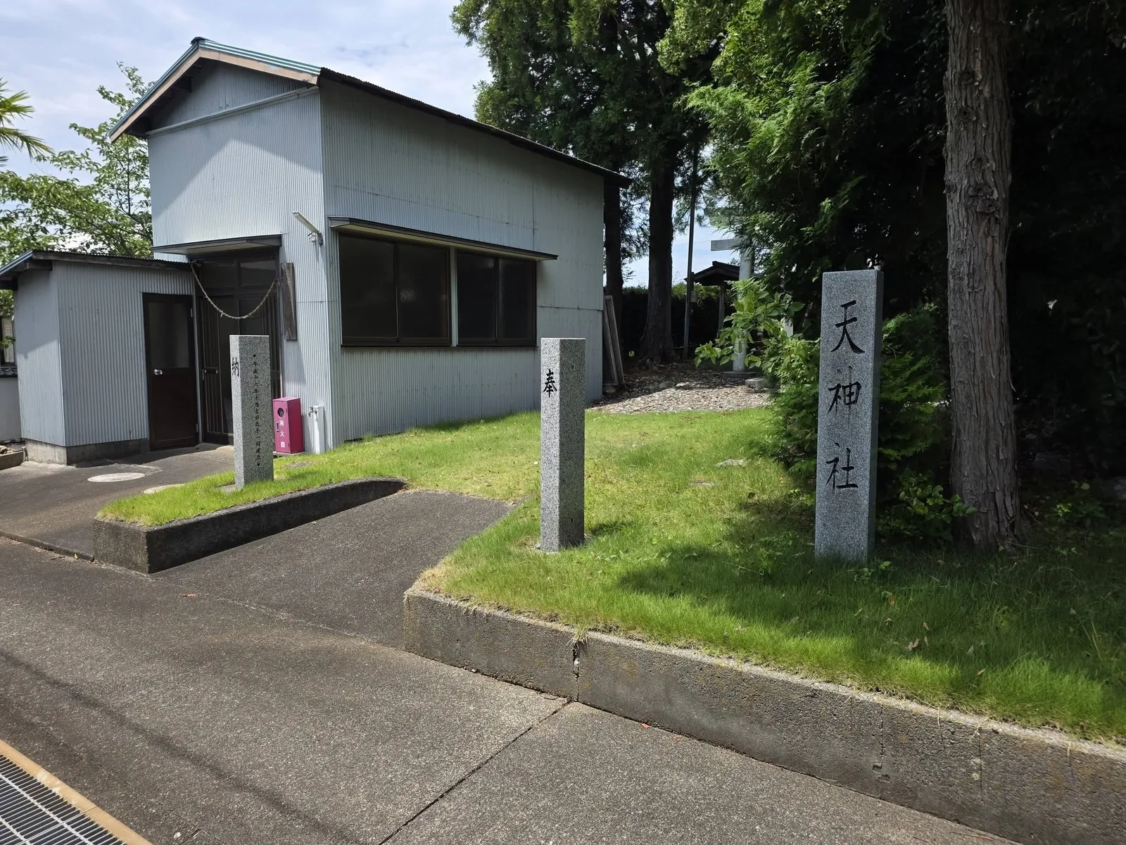 道路から見た境内入口。社号標「天神社」と社叢の大木が立つ。