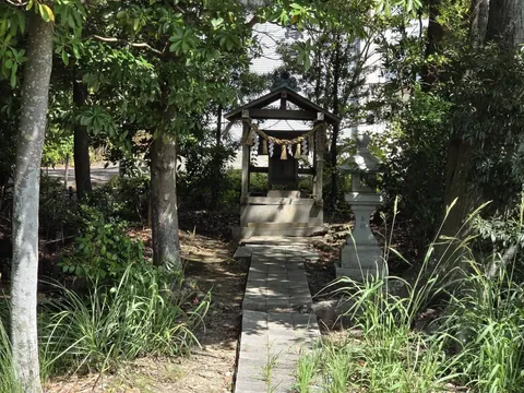 木立の参道奥に立つ小祠と石灯籠。奥に白壁の社殿が見える。