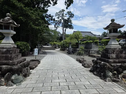 参道入口の一対の献燈と、左手前の「六ツ石」の標識。奥に石段と拝殿が見える。